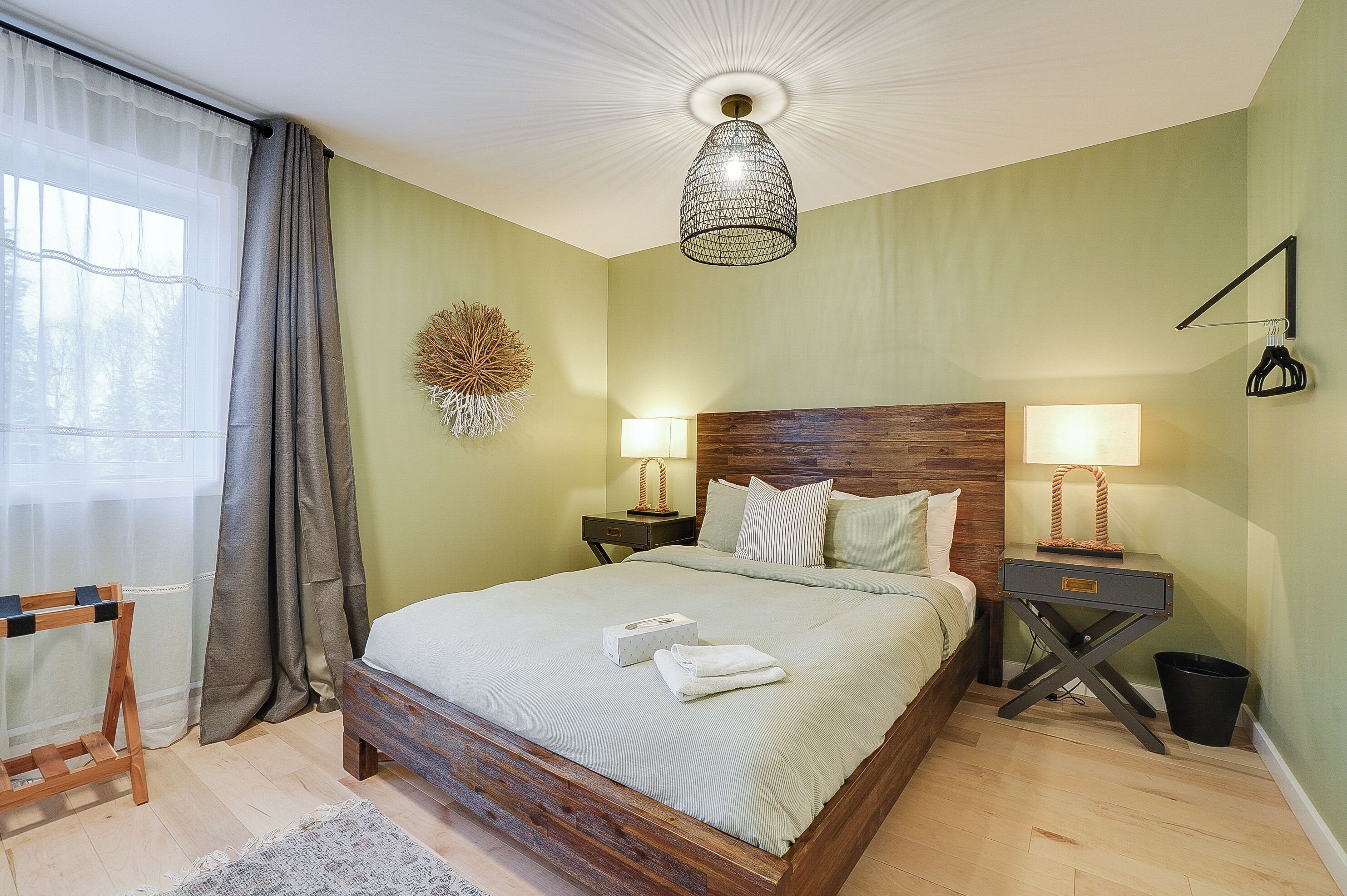 Une chambre à coucher bien aménagée, avec une tête de lit en bois, deux lampes de chevet, une table de chevet, un luminaire suspendu et une fenêtre avec des rideaux.