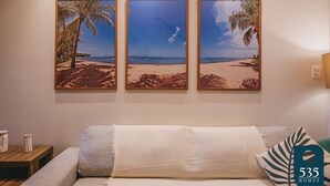 A living room with a beige sofa, a wooden coffee table, and three framed beach paintings on the wall.