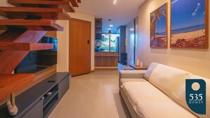 A modern interior with a wooden staircase, a sofa, and a kitchen area visible through an open door.
