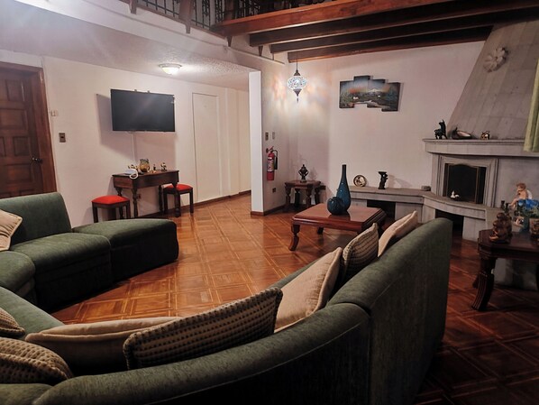 A living room with a fireplace, a television, and a dining area. - Hotel Sweet Garden (Cumbayá)