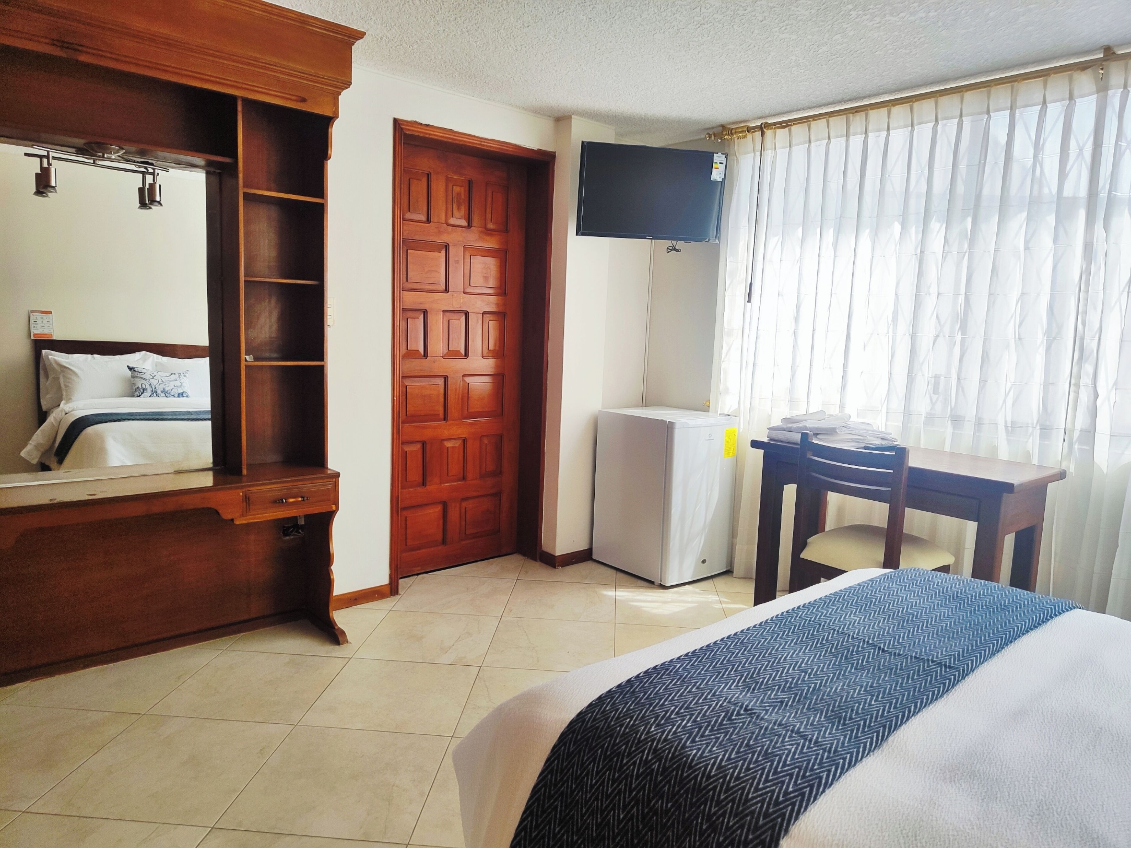 A hotel room with a bed, a desk, a wardrobe, a television, and a window with curtains.