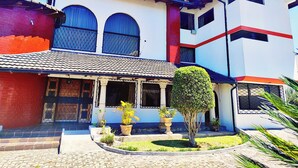 A two-story house with a tiled roof, a red brick section on the left, and a white facade with red and blue accents. - Hotel Sweet Garden (Cumbayá)