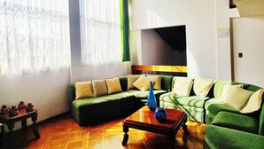 A living room with a green sofa, a wooden coffee table, and a TV mounted on the wall. - Hotel Sweet Garden (Cumbayá)