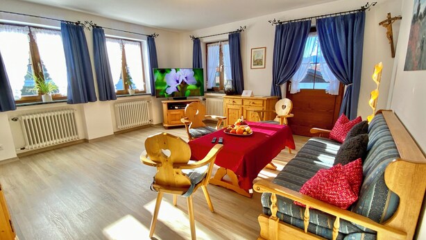 Ein gemütliches Zimmer mit einer Holz-Couch, einem Esstisch mit Obst, einem Fernseher und einer Holzkabine.