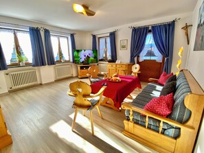A cozy room with a wooden sofa, a dining table with fruit, a television, and a wooden cabinet. - 4-star apartment "Loisach", center of Garmisch with mountain view and balcony (Garmisch-Partenkirchen)