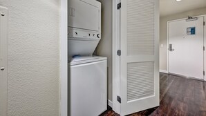 Un cuarto de lavado con lavadora y secadora, una puerta con paneles ventilados y un cartelito en la pared.