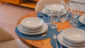 A dining table set with white plates, bowls, cutlery, and wine glasses, with a blue placemat.