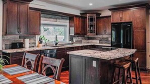 A modern kitchen with dark wood cabinets, a granite countertop, and a central island with stools.