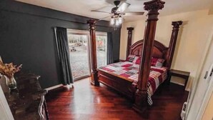 A bedroom with a four-poster bed, a ceiling fan, and a view through a large window.