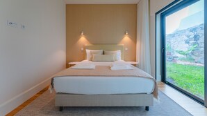 Ein modernes Hotelzimmer mit einem großen Bett, zwei Nachttischen, einer eingebauten Kopfteil und einem großen Fenster mit Blick auf einen Garten.