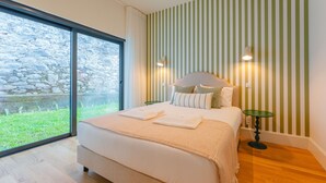 A modern bedroom with a large bed, a view of greenery outside, and a striped wall.