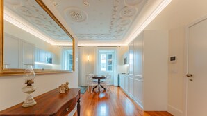Ein geräumiges Zimmer mit Holzboden, einem Esstisch mit Stühlen, einem großen Spiegel und einer Tür.