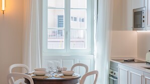 Ein Essbereich mit einem Tisch für vier Personen, einem Fenster mit Vorhängen und einer Küche mit weißen Schränken und einer Mikrowelle.