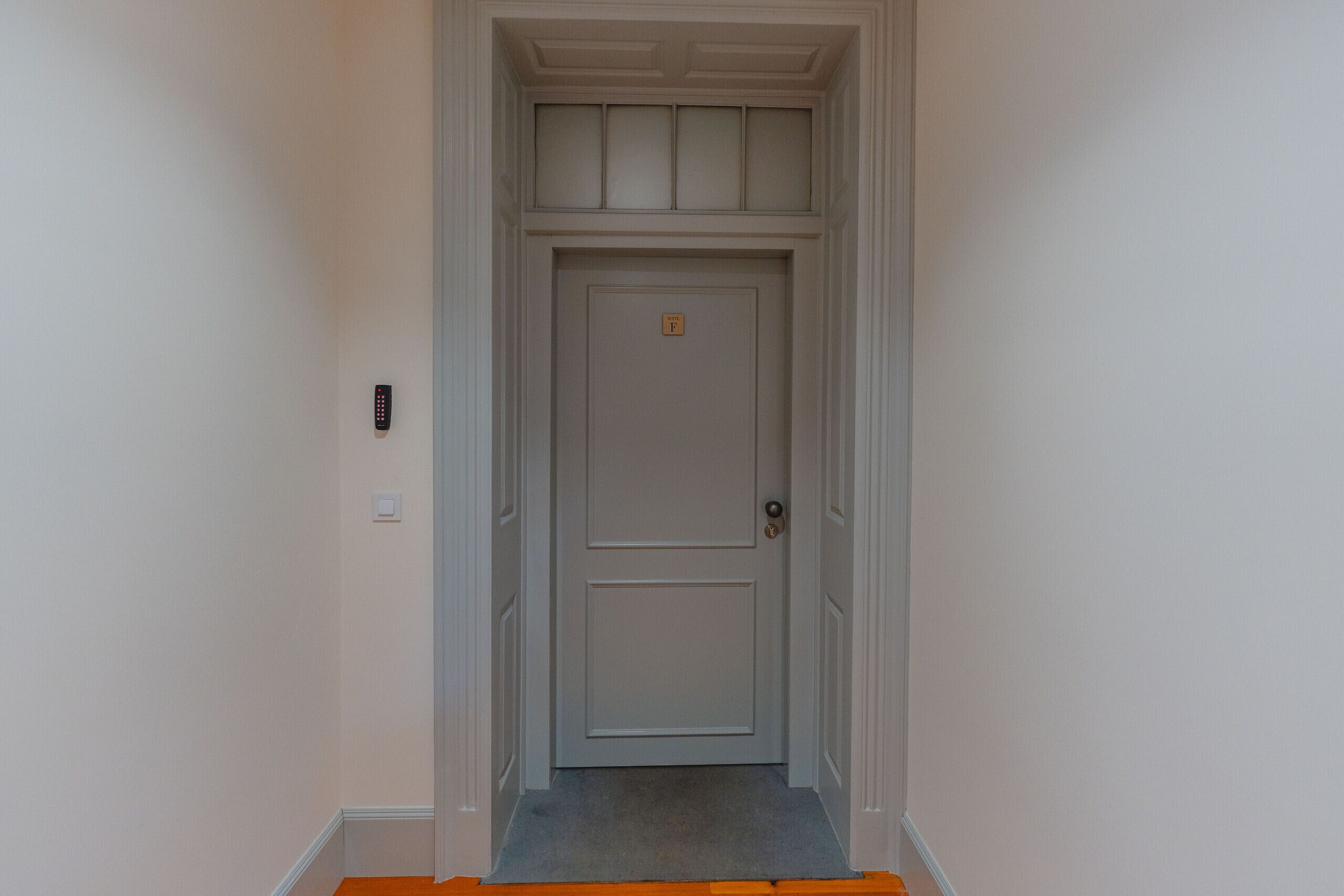 A narrow hallway with a door at the end, a light switch, and a remote control on the wall.