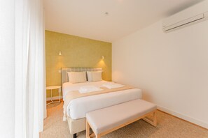 Une chambre à coucher bien rangée, avec un lit, des tables de chevet, un banc et un appareil de climatisation.