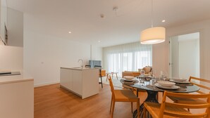 A modern kitchen with a central island, a dining area with a round table, and a living space with a sofa and a TV.