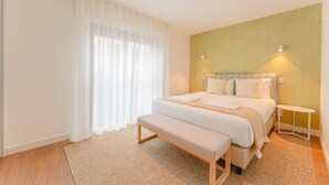 A bedroom with a bed, bench, bedside table, and a wall-mounted light fixture.