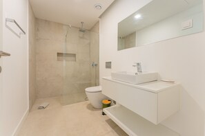 Une salle de bain moderne avec une douche à parois de verre, des toilettes et un meuble-lavabo blanc avec un miroir.