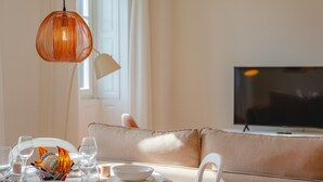 A dining area with a round table set for a meal, a television in the background, and a sofa with cushions.