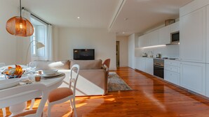A modern living room with a dining area, a sofa, and a kitchen with white cabinets and appliances.