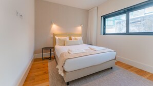 A modern bedroom with a large bed, a small bedside table, a window with curtains, and a light-colored wall. - FLH Funchal A Quinta do Conde Balcony Flat VI (Funchal)