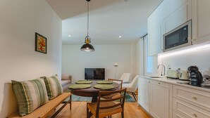 Eine moderne Küche mit weißen Schränken, einem Esstisch mit grünen Platzsets, einer Bank und einem Fernseher im Hintergrund.