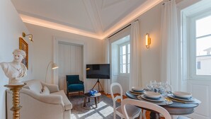 A living room with a sofa, a table set for dining, a TV, and a statue. - FLH Funchal A Quinta do Conde Suite II (Funchal)