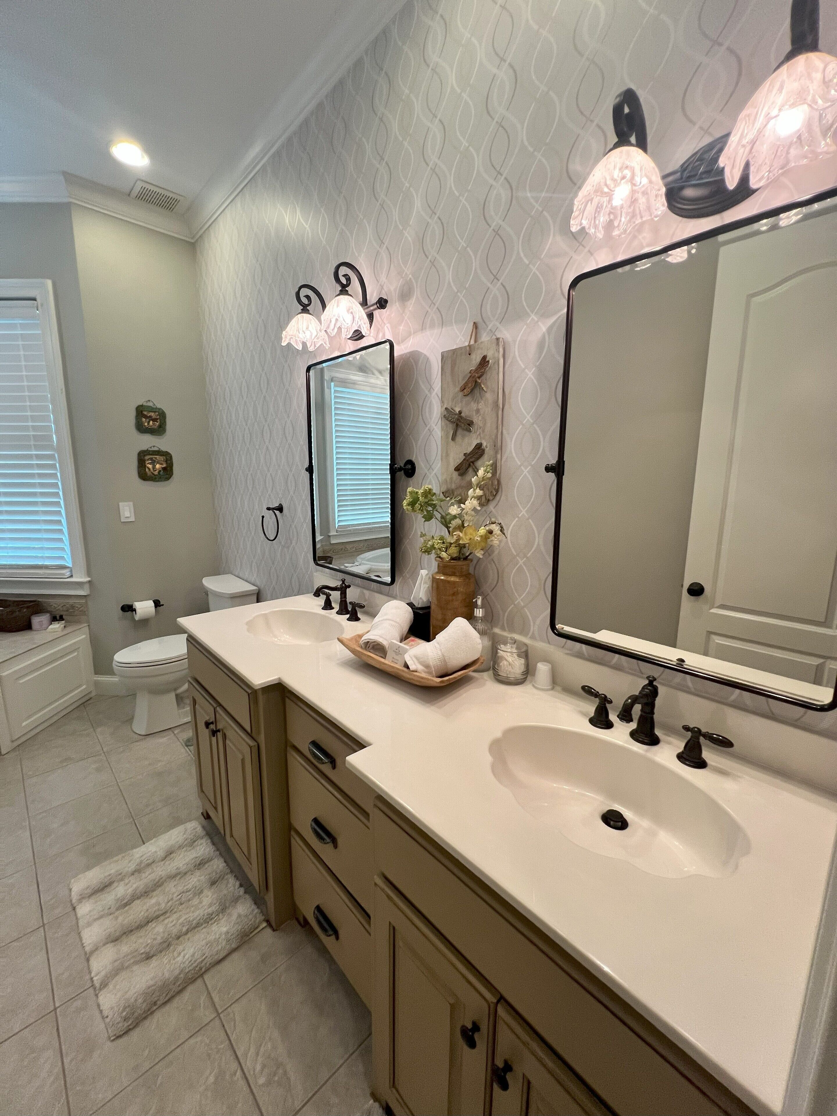 A bathroom with two sinks, a toilet, a vanity with drawers, a mirror, and decorative wall elements.