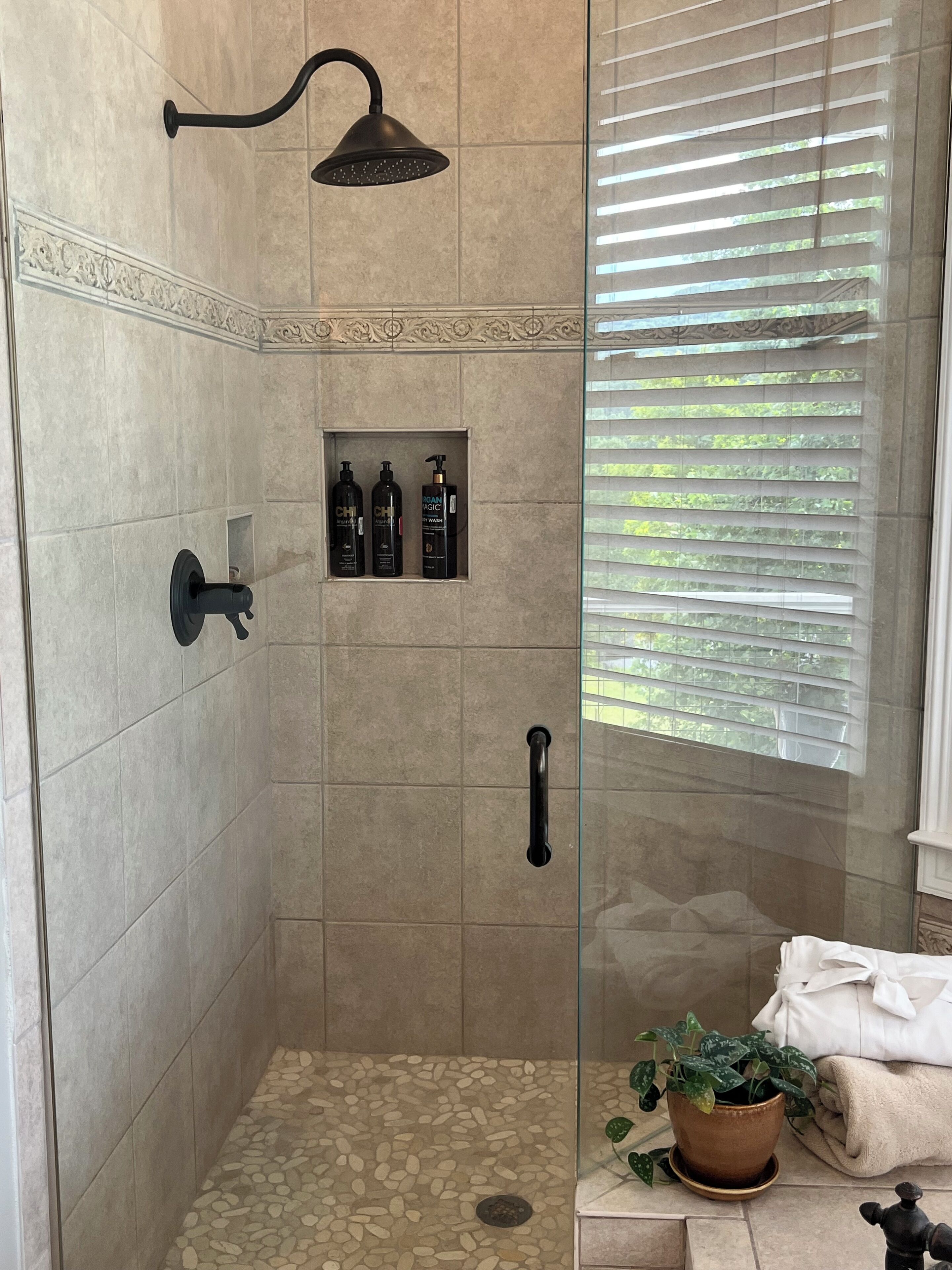 A shower area with a glass door, a showerhead, and a shelf with toiletries.