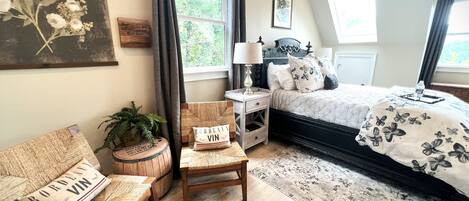 A bedroom with a bed, bedside table, chair, and a large window with curtains.