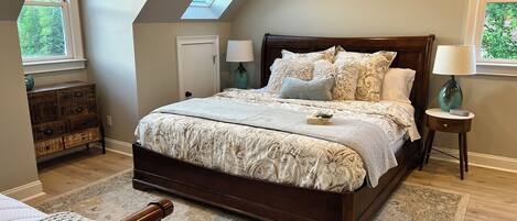 A bedroom with a large bed, a skylight, a dresser, and two bedside lamps.
