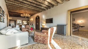 Un salon spacieux avec un plafond haut, une cheminée, un canapé, un fauteuil à motifs et un téléviseur.