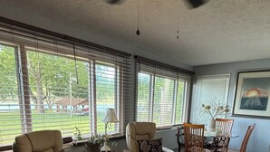 Un salón amplio con un gran ventanal, ventilador de techo y comedor con sillas y mesa de madera.