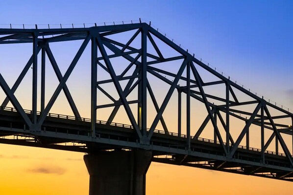 Un puente de acero con estructura de celosía que cruza un cuerpo de agua durante la puesta de sol.