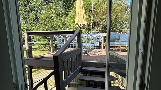 Una escalera de madera que sale al exterior, con barandilla de metal, un paraguas amarillo y asientos al aire libre.