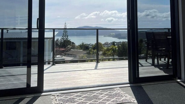 A balcony with a view of the sea and mountains, a clock on the wall, and a doormat on the floor.