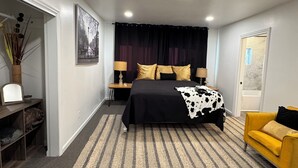 Ein Schlafzimmer mit einem Bett, einem Nachttisch, einer Lampe, einem Sessel und einer Tür.