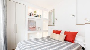 Un dormitorio con cama, armario, estantería con libros, un cuadro enmarco y un espejo.