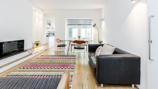 Una sala moderna con un sofá oscuro, un televisor y un comedor con mesa y sillas.