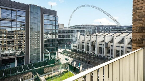 A modern building with large windows and a glass facade, surrounded by greenery and a road. - Wembley Empire Apartment - City Living (Wembley)