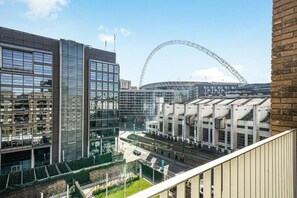 A modern building with large windows and a glass facade, surrounded by greenery and a road. - Wembley Empire Apartment - City Living (Wembley)