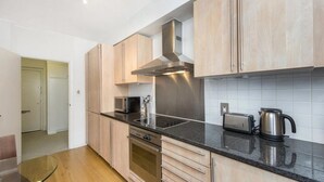 A modern kitchen with light wood cabinets, a stainless steel range hood, a built-in oven, a microwave, a toaster, and a kettle on the countertop. - Wembley Empire Apartment - City Living (Wembley)