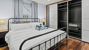 Quarto moderno com estrutura de cama em metal, guarda-roupa espaçoso e mesa de cabeceira com abajur.