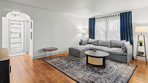 Uma sala de estar moderna com um sofá cinzento, duas mesinhas laterais, uma mesa de centro redonda e um tapete estampado.