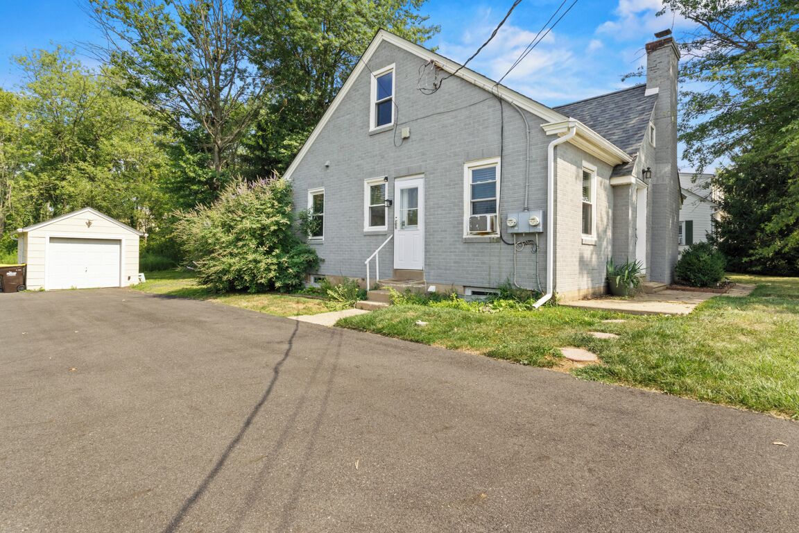 Une maison à deux étages avec un garage, un porche à l’avant et un petit abri de jardin.