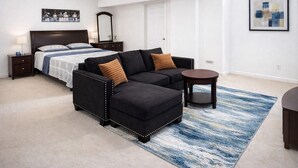 Une chambre à coucher comprenant un lit, un canapé d’angle noir, une petite table ronde et un tapis bleu à motifs.