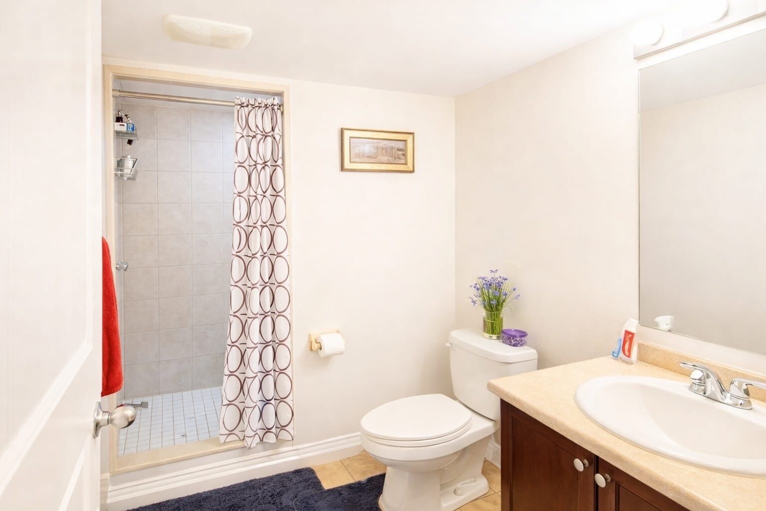 Une salle de bain équipée d’une douche, de toilettes, d’un lavabo et d’un tableau encadré au mur.