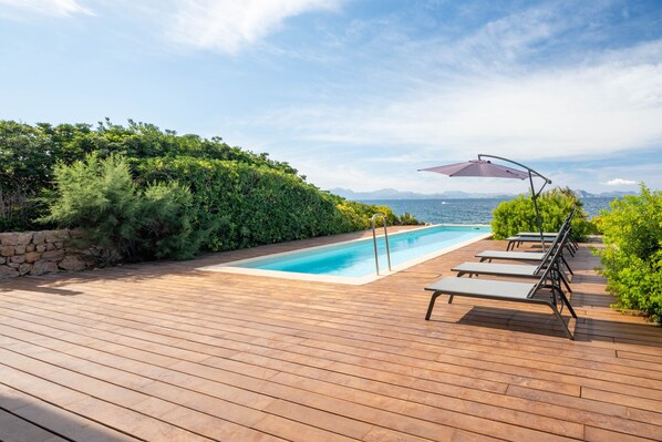 Une terrasse en bois avec une piscine, des chaises longues et une vue sur la mer.