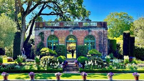 A historic building with arched windows and a brick facade, surrounded by well-maintained gardens and a reflecting pool.