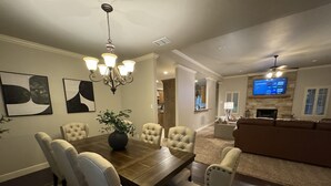 A dining area with a wooden table and six upholstered chairs, a chandelier, and two abstract paintings on the wall. - Fountain Hills Grandeur (Lubbock)